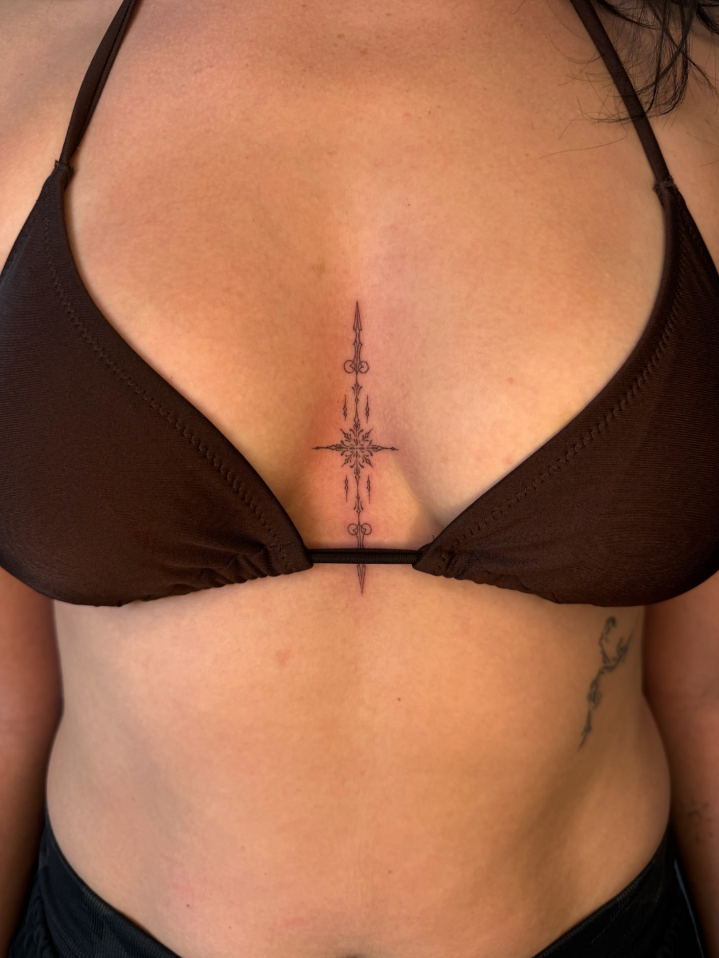 Ornamental fine line sternum tattoo between a brown bikini top