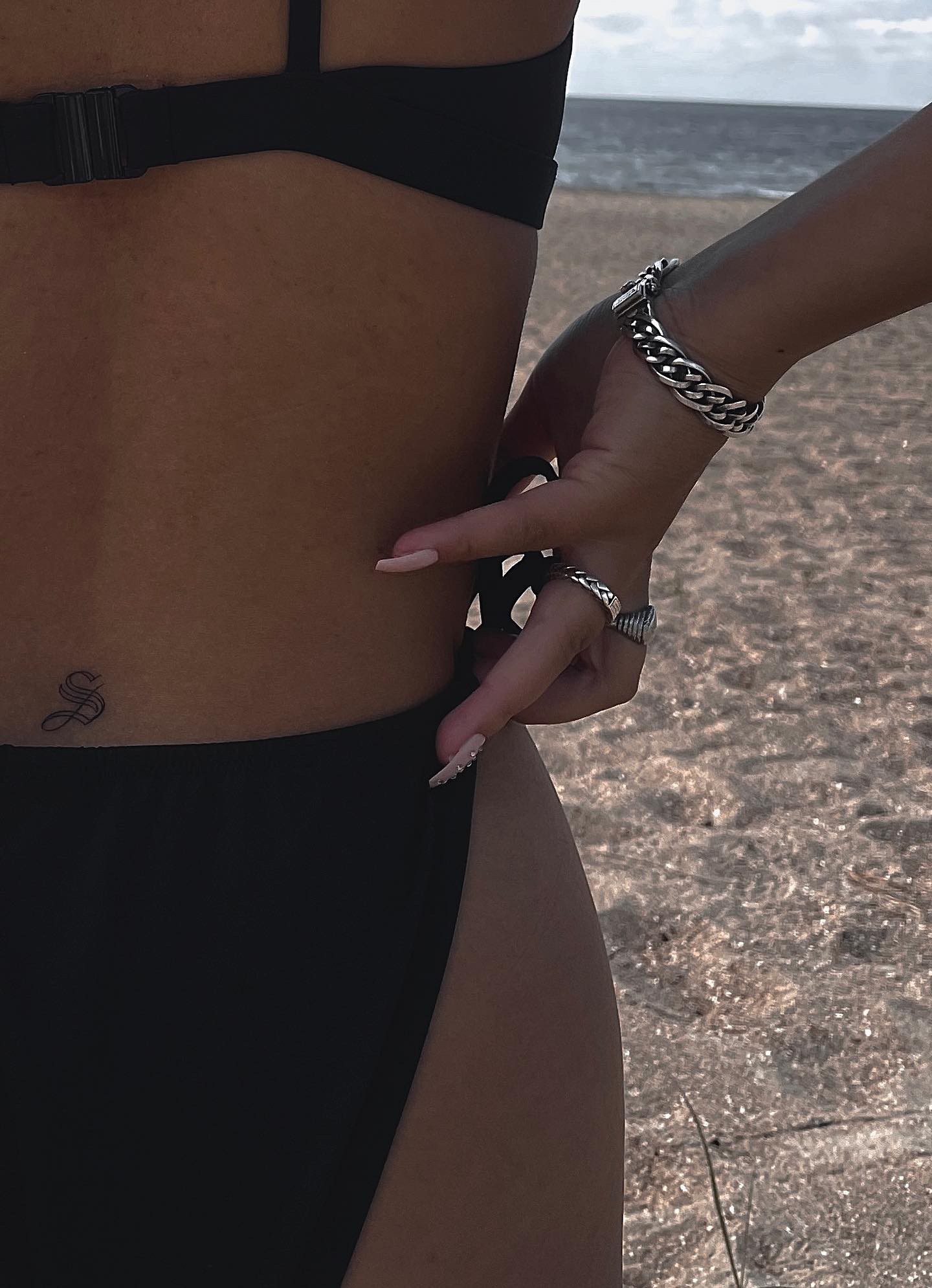 Small ornamental letter tattoo on the lower back at the beach