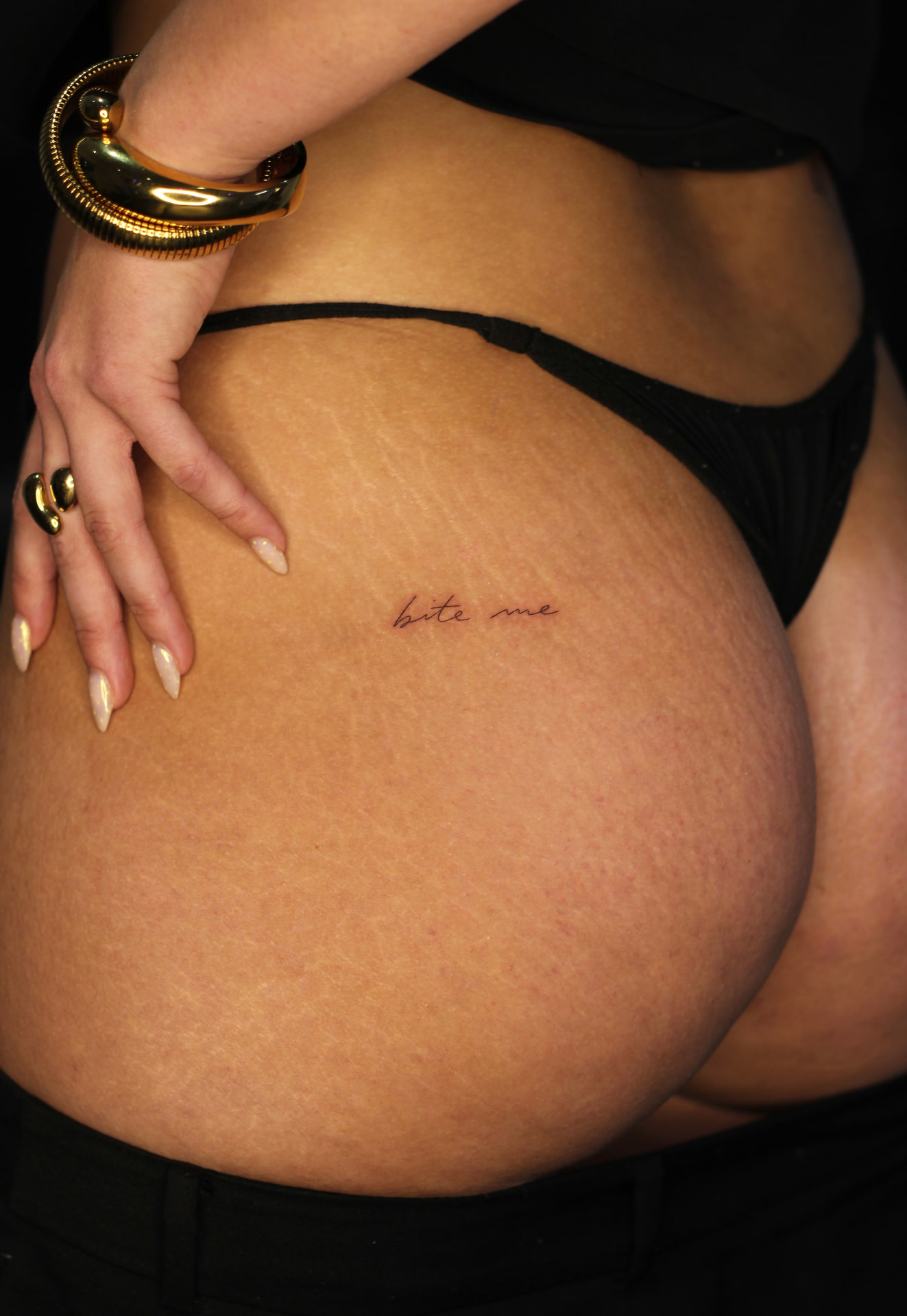 Fine line script tattoo 'bite me' on the hip with gold jewellery