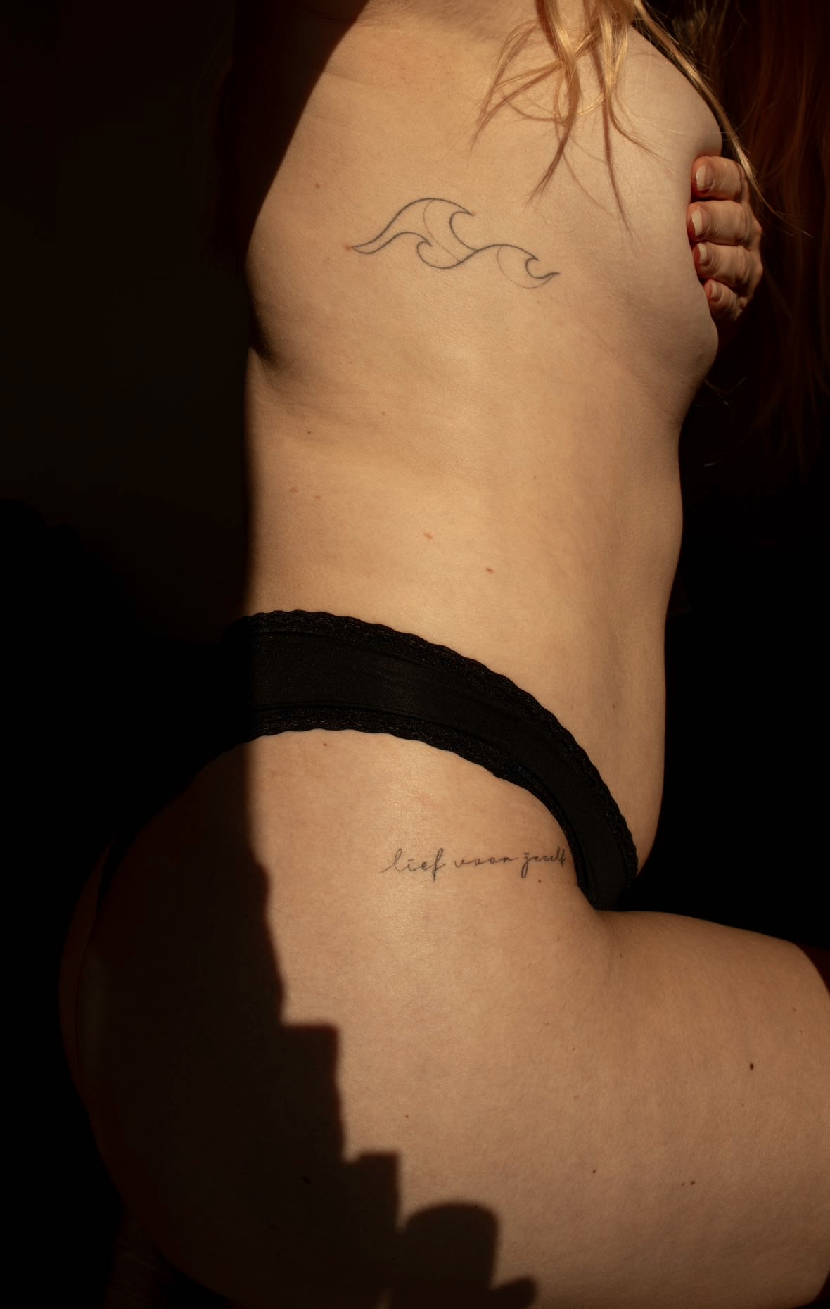 Fine line wave and script tattoo along the torso in warm light