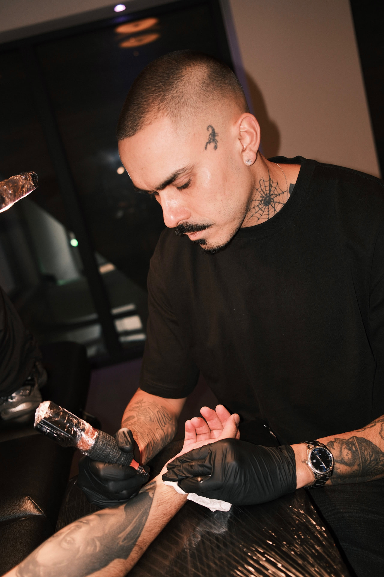 66onions tattooing a forearm at night, machine in hand