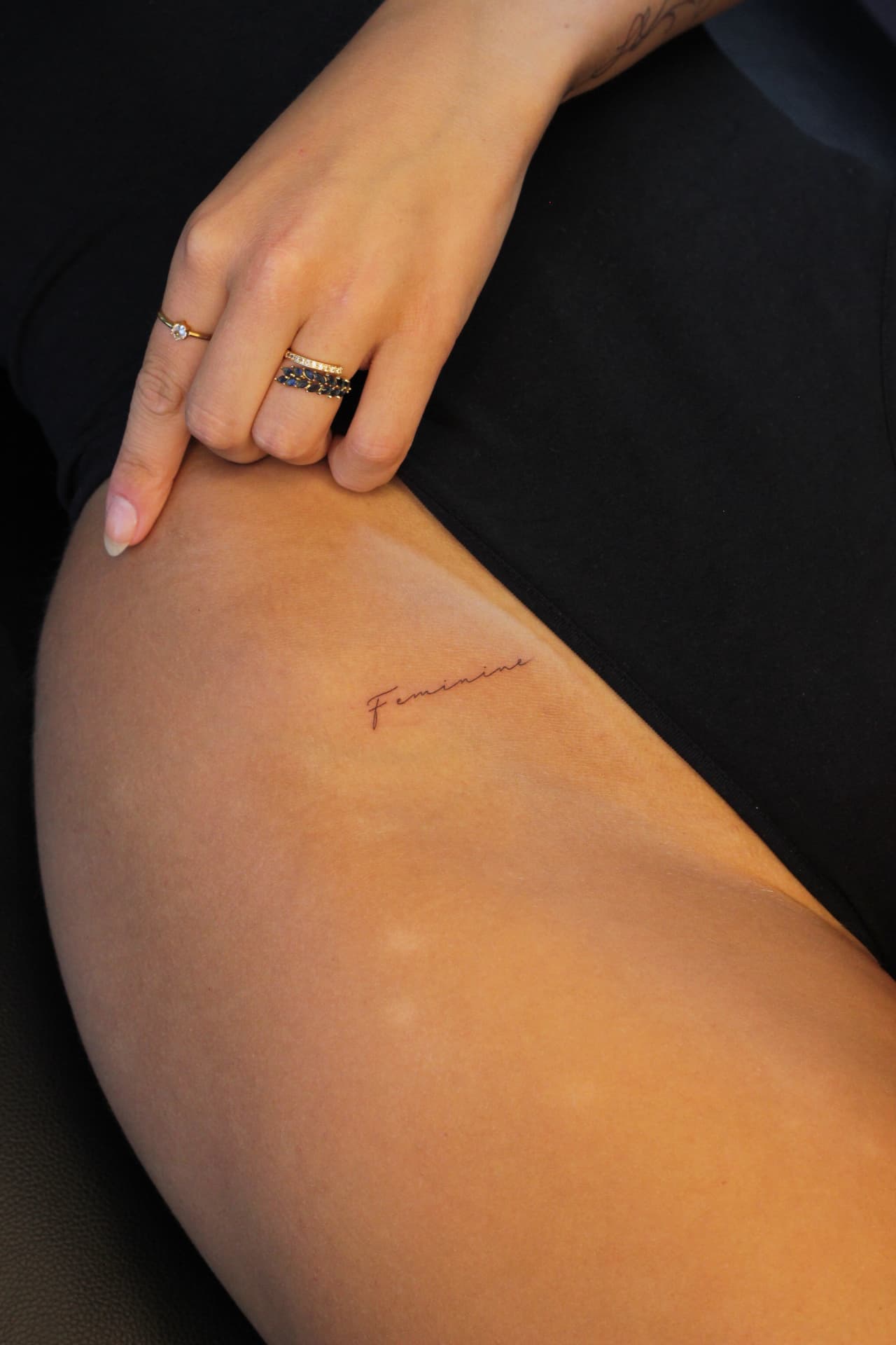 Delicate script tattoo reading Feminine on the thigh