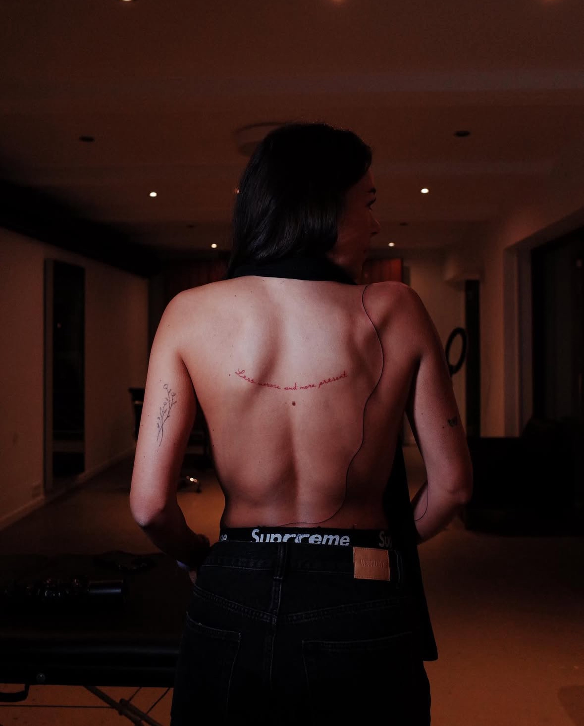 Red ink script tattoo along the back in low light